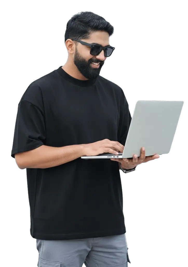 A man in a black t-shirt and sunglasses working intently on his laptop in a casual setting.